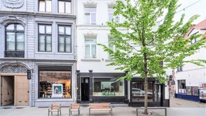 A street view with a building featuring a shop named 'Necessities' and a tree in the foreground. - Apartment in Fashion Street Residence (Antwerp)