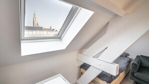 A loft bedroom with a skylight, a bed, a green sofa, and a view of a tower. - Cosy 1-bedroom apartment, Antwerp (Antwerp)