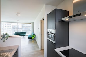 Uma cozinha moderna com forno embutido, exaustor escuro e vista para a cidade através de grandes janelas.