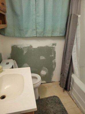 Ein Badezimmer mit Toilette, Waschbecken und einer teilweise gestrichenen Wand.