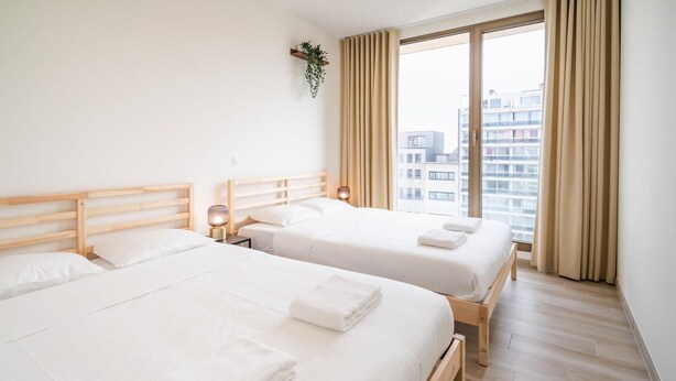 A hotel room with two beds, a large window, and a view of buildings. - Urban Family City Escape in Antwerp (Antwerp)