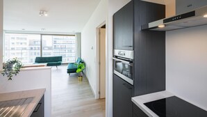 A modern kitchen with a built-in oven, a dark-colored range hood, and a view of a cityscape through large windows. - Urban Family City Escape in Antwerp (Antwerp)