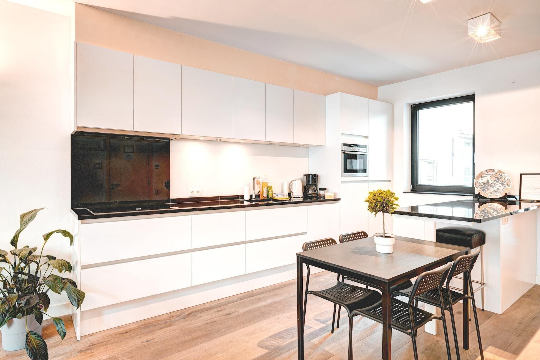 Een moderne keuken met witte kasten, een zwart aanrecht en een eethoek met een houten tafel en stoelen.