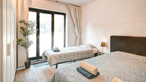 Habitación de hotel con dos camas, una planta en maceta, una ventana con cortinas y una lámpara de noche.
