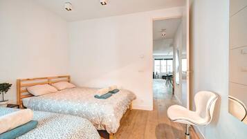 Un dormitorio con dos camas, una silla y vista hacia un comedor.