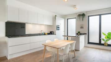 A modern kitchen with white cabinetry, a black countertop, and a wooden dining table with chairs.