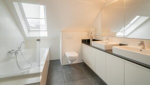 Un baño moderno con tragaluz, una bañera, un inodoro y dos lavamanos.