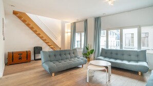 Una sala de estar moderna con una escalera de madera, dos sofás grises, una mesita blanca y una planta en maceta.
