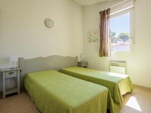 A room with two beds, a nightstand, a lamp, a wall clock, a window with curtains, and a radiator. - Beautiful Holiday Home Near Vineyards (Aubignan)