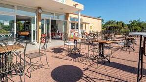 An outdoor cafe area with tables and chairs, a building entrance, and a sign above. - Beautiful Holiday Home Near Vineyards (Aubignan)