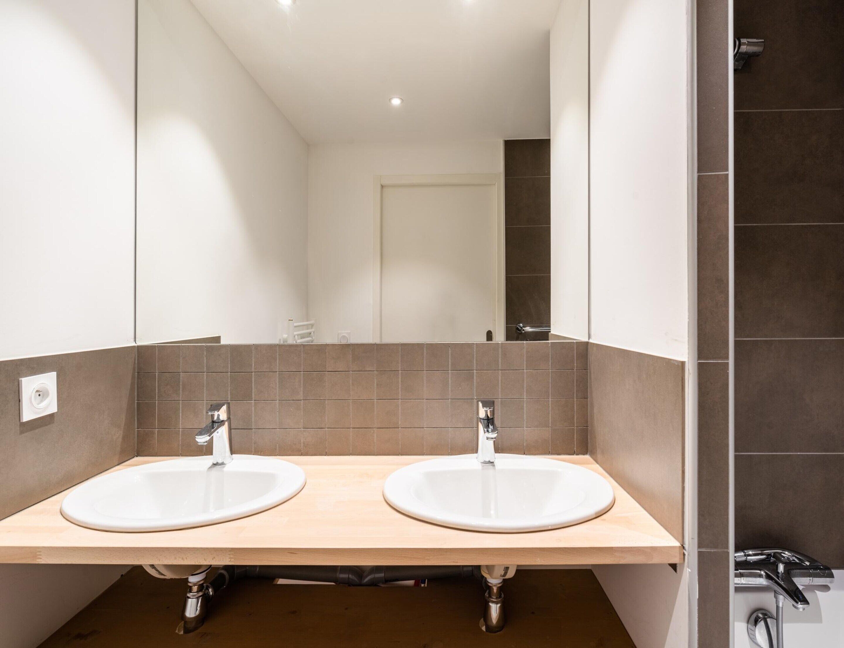 A bathroom with two sinks, a mirror, and a shower area.