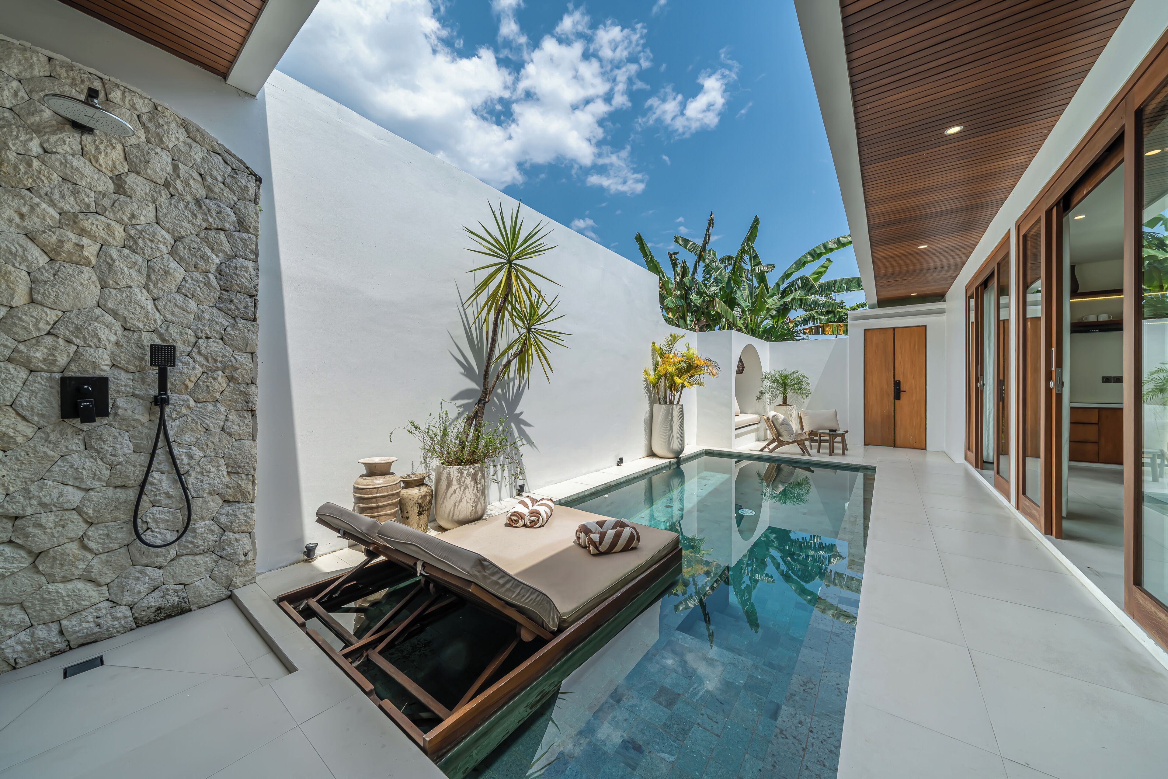 Un espace piscine extérieur moderne, agrémenté d’un mur en pierre, d’un plafond en bois et de plantes en pot.