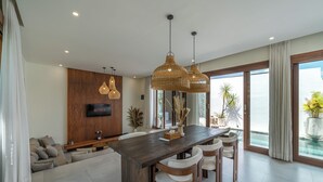Una sala de estar moderna con un gran comedor de madera, asientos cómodos, un televisor de pantalla plana y ventanas amplias que ofrecen vistas al exterior.