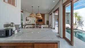 Una cocina moderna con encimera de mármol, comedor y vista a una piscina.