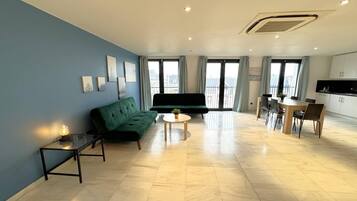 A modern living room with a green sofa, a small round table, and a dining area with a wooden table and chairs.