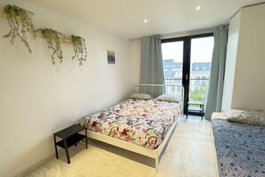 Ein Schlafzimmer mit Bett, kleinem Tisch, einem Balkon mit Blick und hängenden Pflanzen.