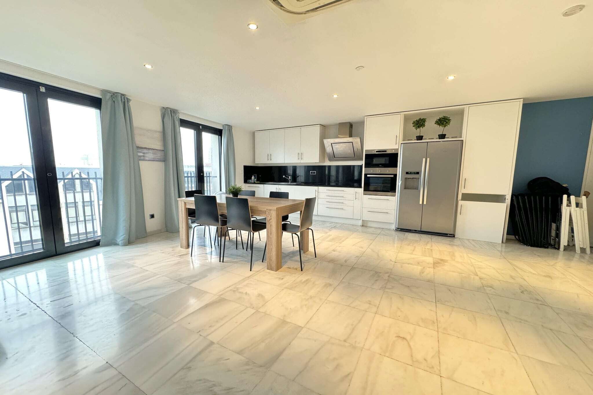 A modern kitchen with a dining area, large windows, and a view of the outside.