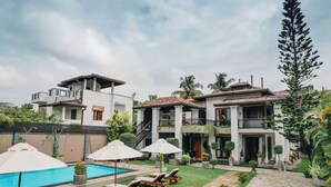 Una villa moderna con piscina, sillas de descanso y un jardín bien cuidado.