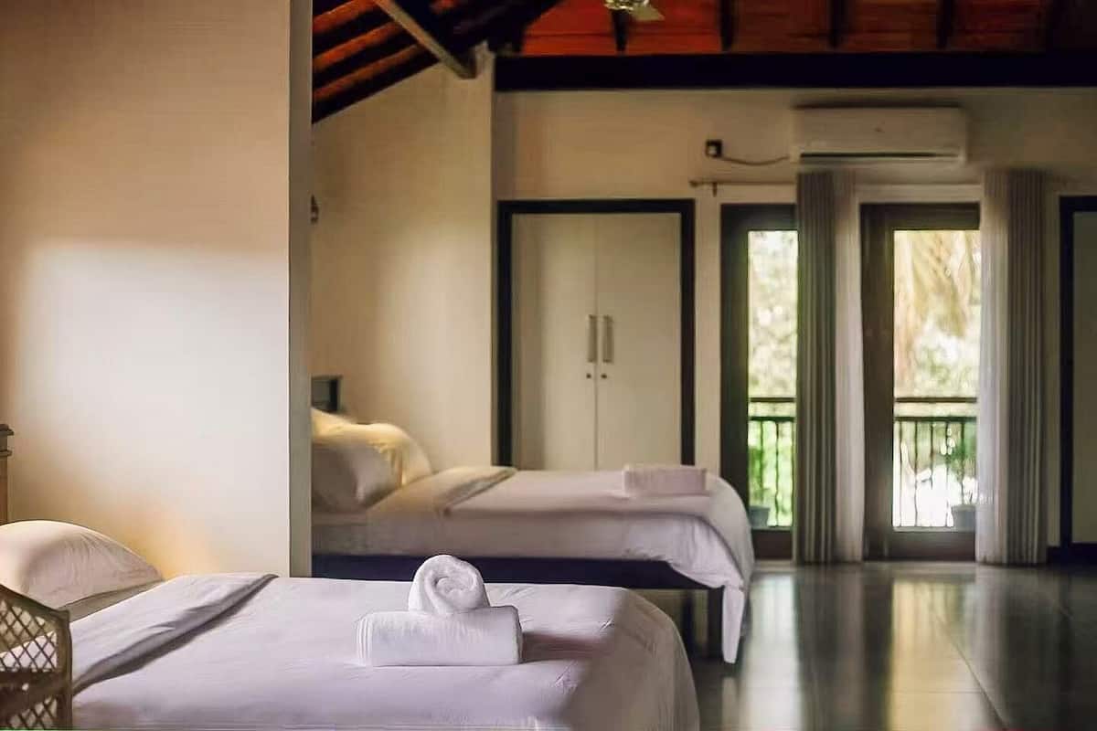 A hotel room with two beds, a balcony, and a view of the outdoors.