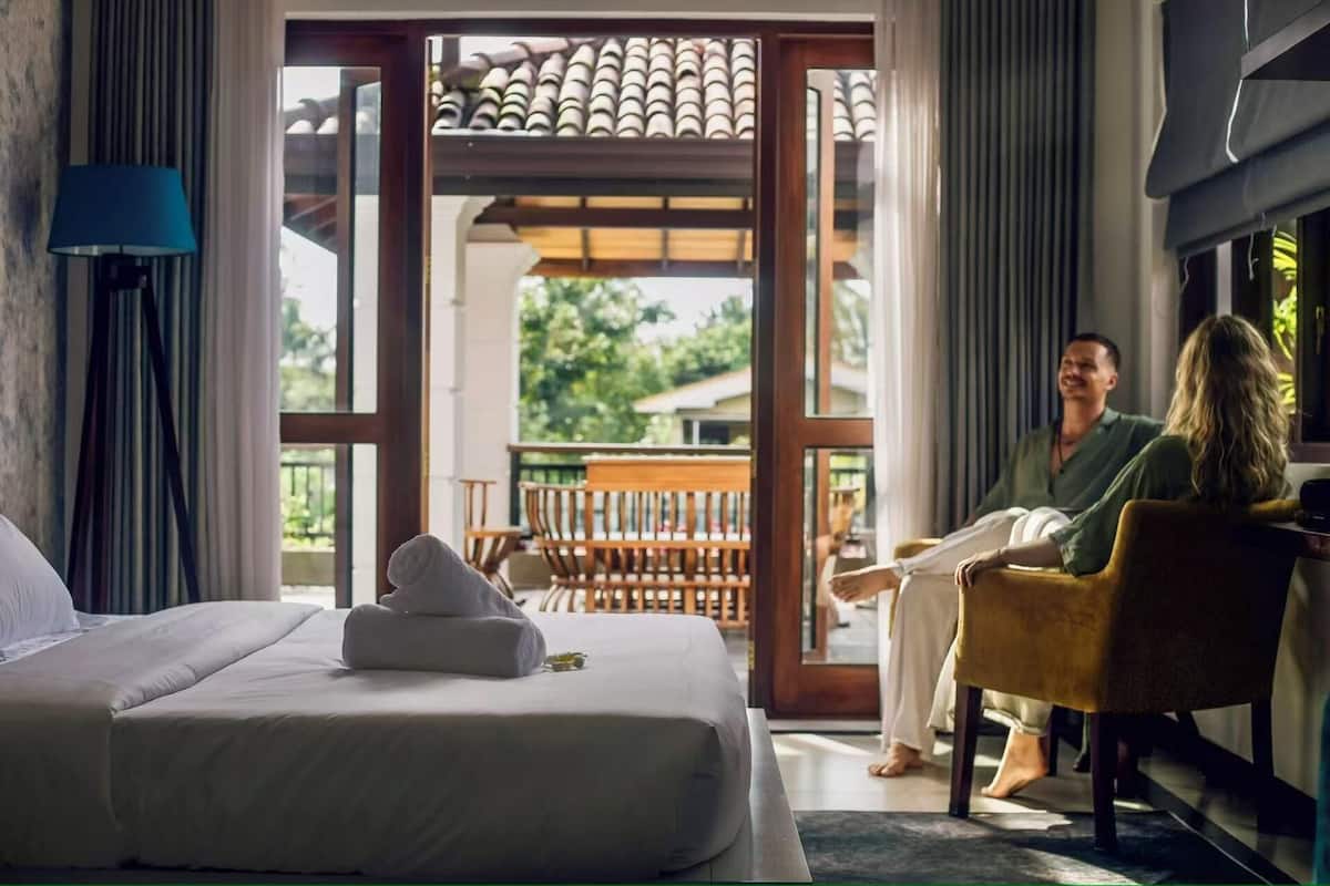 A hotel room with a bed, a sitting area with a chair, and a view of the outdoors.