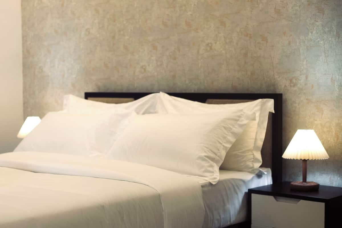 A neatly made bed with white linens, a wooden headboard, and a bedside table with a lamp.