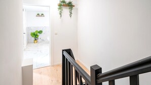 A staircase with a black railing, a white door leading to a bathroom with a marble floor, and a hanging plant.