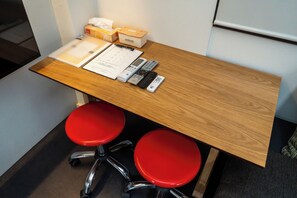 Un bureau en bois avec un bloc-notes, un stylo, des télécommandes et une boîte de mouchoirs.