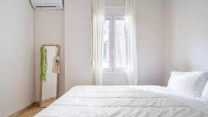 A bedroom with a bed, a window with curtains, a bedside plant, and a wall-mounted air conditioner. - STM Monastiraki Acropolis Apt (Athina)