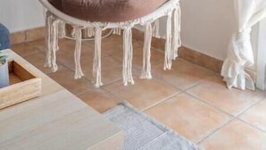 A macrame hanging chair with a brown cushion in a room with tiled flooring and a framed floral artwork on the wall. - STM Monastiraki Acropolis Apt (Athina)