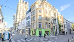 Un immeuble à plusieurs étages avec une devanture verte portant l’inscription « DELI BOX », un passage pour piétons et un feu de signalisation pour piétons.
