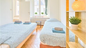 Une chambre avec deux lits, une fenêtre avec des plantes, un radiateur et une étagère sur laquelle se trouve une plante.