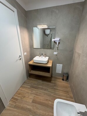 Un baño moderno con tocador de madera, un espejo grande, ducha integrada y bañera separada.