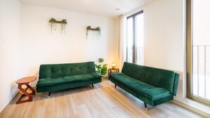 Ein Zimmer mit zwei grünen Sofas, einem kleinen Holztisch, einer Zimmerpflanze und einem Fenster mit Blick.