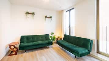 Una habitación con dos sofás verdes, una pequeña mesa de madera, una planta en maceta y un ventanal con vistas.