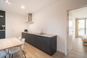 Una cocina moderna con una isla central, una mesa de comedor con sillas y vistas a un dormitorio.
