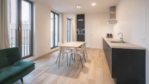 Eine moderne Küche mit einer zentralen Kochinsel, einem Essbereich mit Tisch und Stühlen sowie einem grünen Sofa.