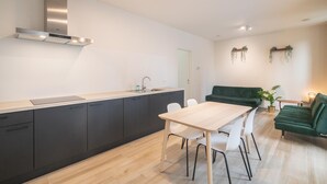 Eine moderne Küche mit Einbauherd, ein Essbereich mit Tisch und Stühlen sowie ein grünes Sofa in einem Wohnraum.