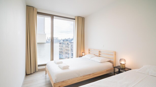 Ein Schlafzimmer mit großem Fenster, einem Bett, einem Nachttisch mit Lampe und einem weiteren Bett.