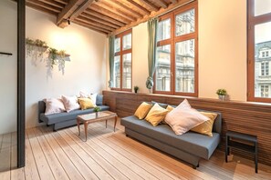 Un salon moderne doté d’un plancher en bois, de deux canapés avec des coussins, d’une table basse et de grandes fenêtres avec des rideaux.