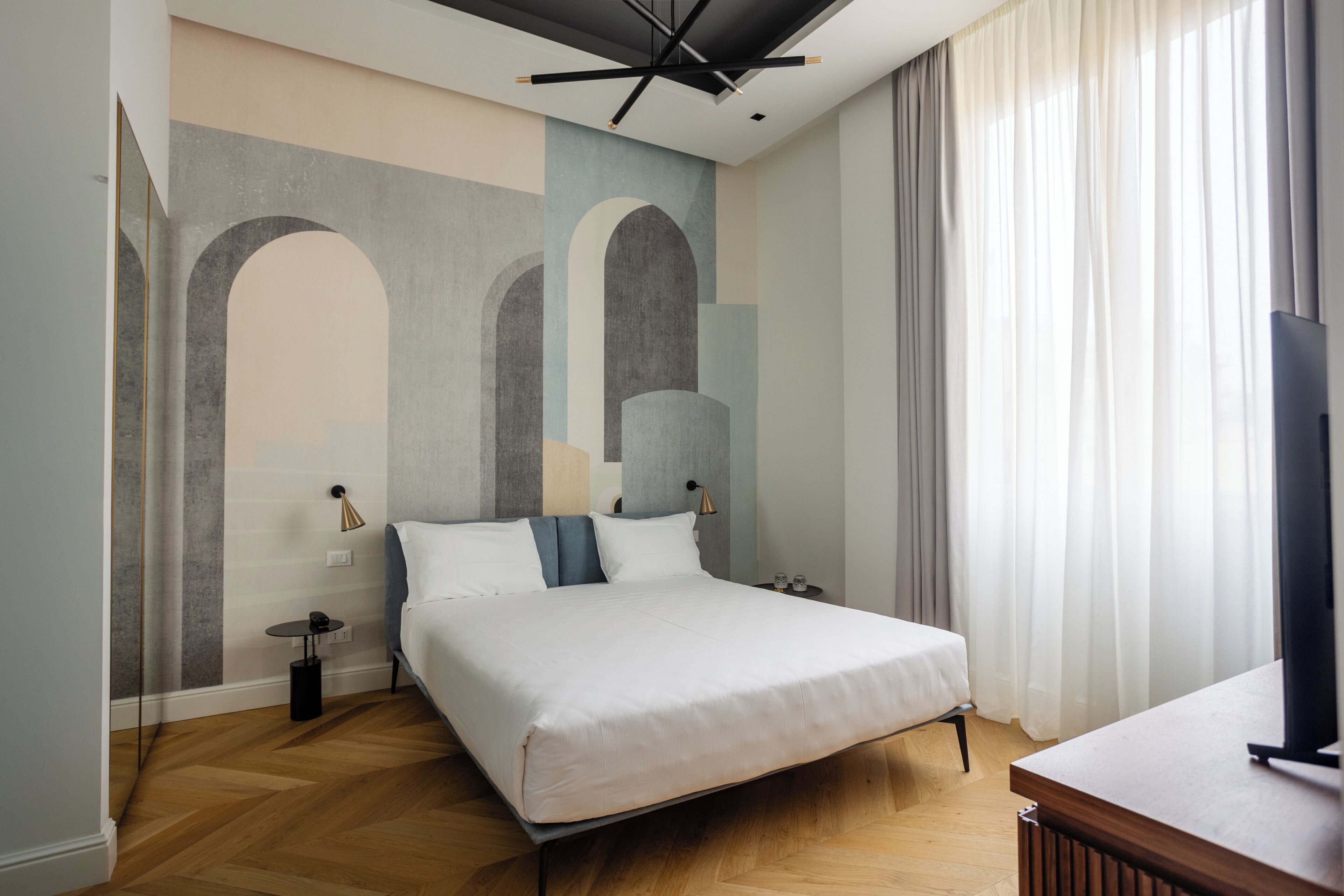 A modern hotel room with a large bed, a flat-screen TV, a small bedside table, and a wall with abstract art.