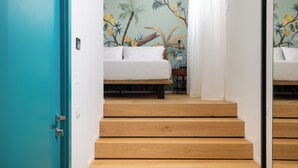 A staircase leading to a bedroom with a white bed, a teal door, and a mural of tropical plants. - Atelier Alinari Rooms (Florence)