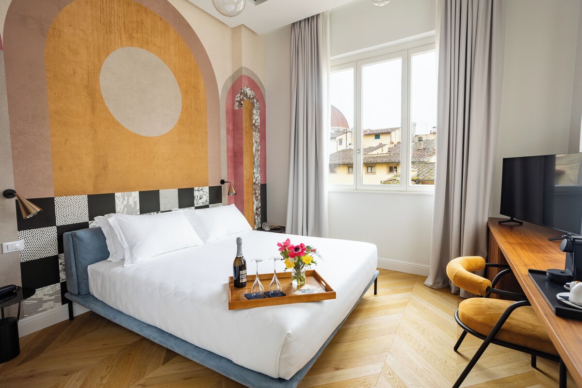 Ein Hotelzimmer mit Bett, Schreibtisch, Fernseher und Fenster mit Blick auf Gebäude.