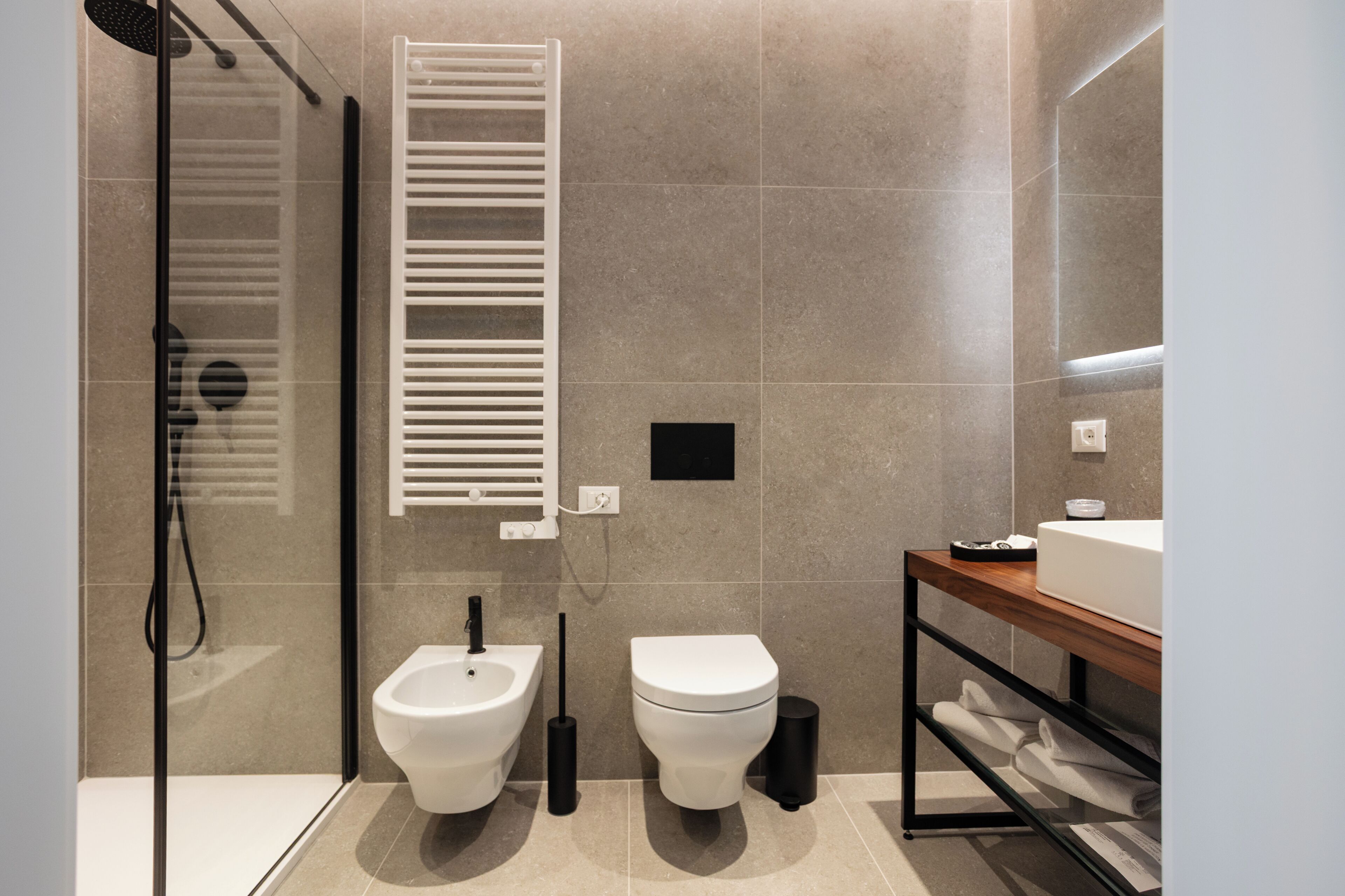 A modern bathroom with a shower, bidet, toilet, and a wooden vanity with a mirror.