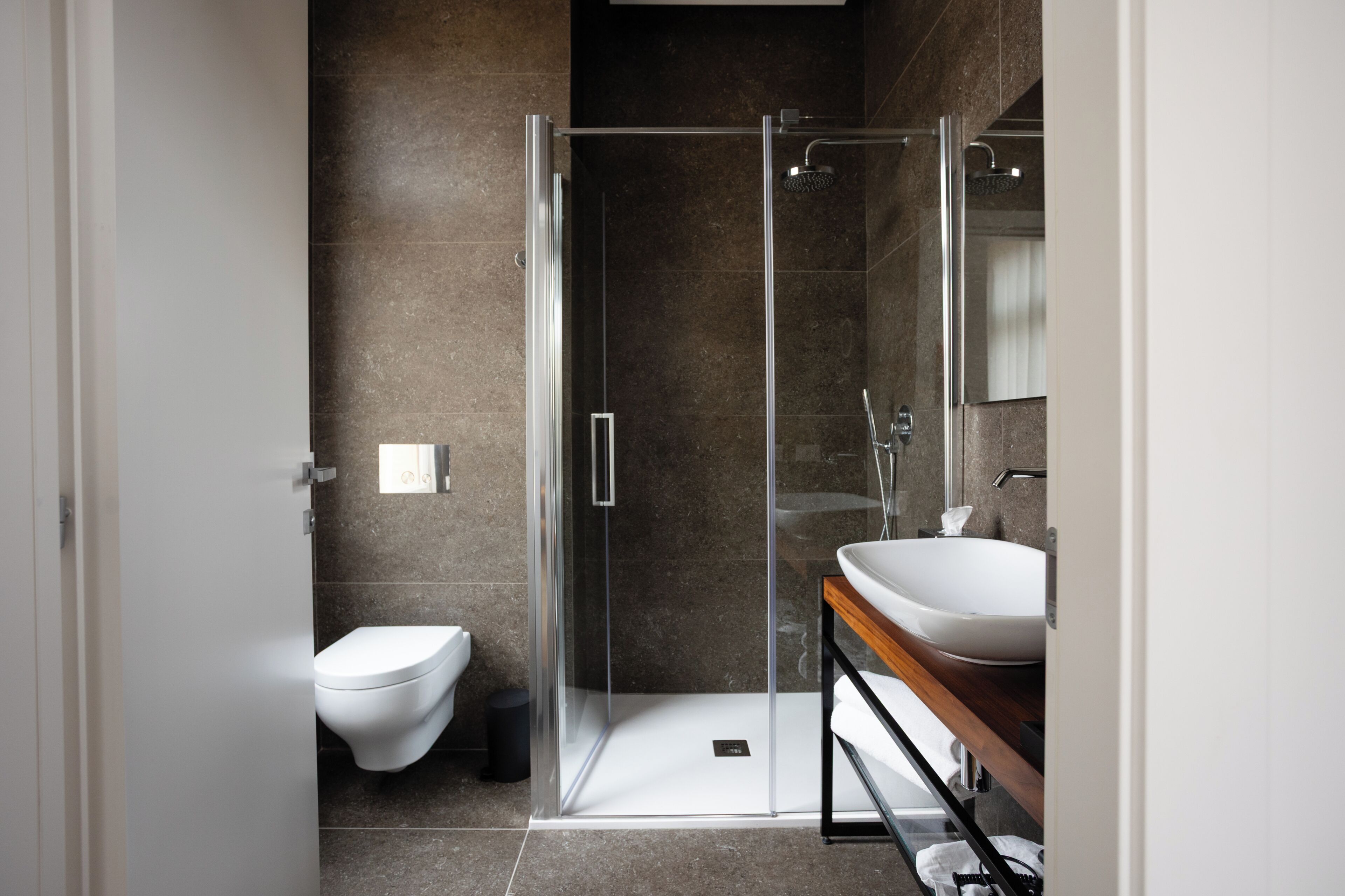 A modern bathroom with a glass-enclosed shower, a white toilet, and a wooden vanity with a white sink.