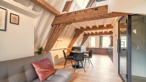 Ein Loft-Zimmer mit Holzbalkendecke, einer Couch, einem Esstisch mit Stühlen und einer Schiebetür aus Glas.