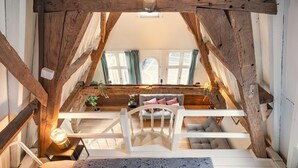 Ein Schlafzimmer im Loft-Stil mit einer Holztreppe, einem Bett mit gemusterten Bettwaren, einem kleinen Tisch mit einer Lampe und Blick auf das Wohnzimmer darunter.
