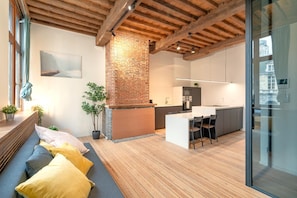 Eine moderne Küche mit Kamin aus Ziegelsteinen, Holzboden und Essbereich mit Bank und Kissen.