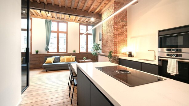 A modern kitchen with a large island, a built-in oven, and a brick accent wall. - Apartment for 6 with Antwerp City Views (Antwerp)