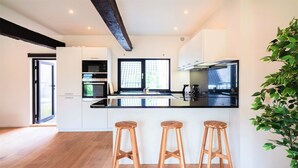 A modern kitchen with a black countertop, wooden stools, and built-in appliances.