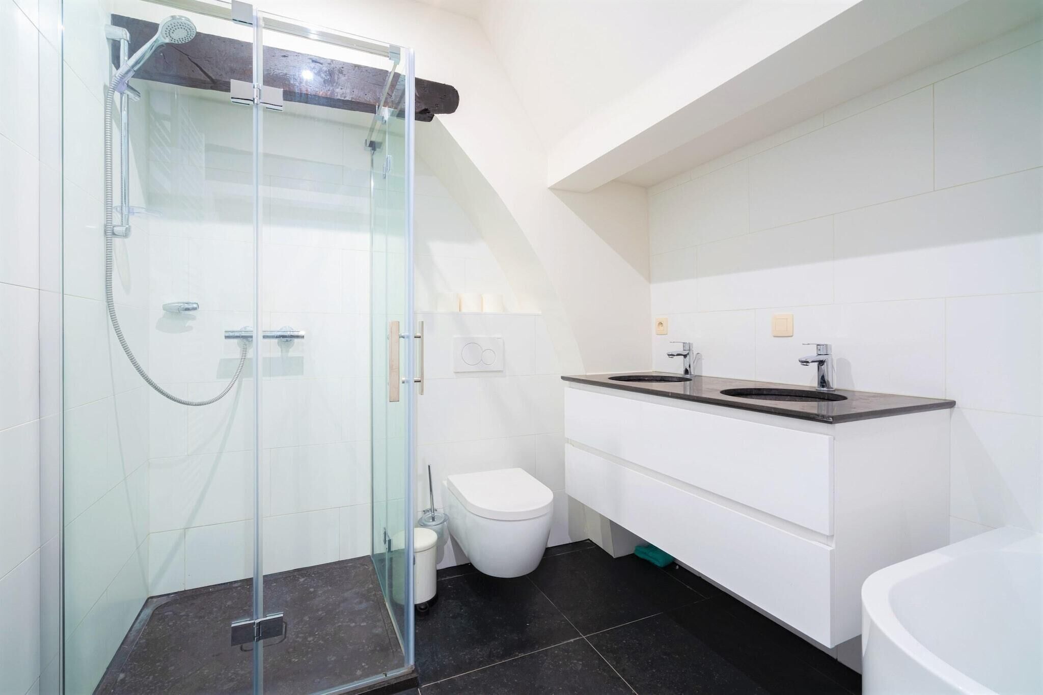 Une salle de bain moderne avec une douche à parois de verre, des toilettes blanches, un meuble-lavabo à deux vasques et une baignoire.